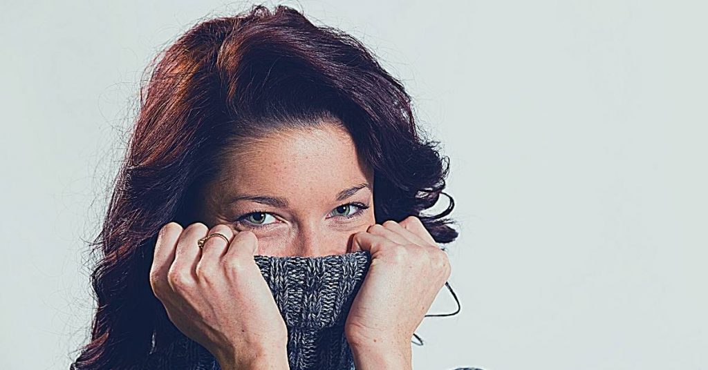a person covering their mouth with a knitted scarf, emphasizing oral area discomfort or concern