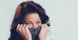 a person covering their mouth with a knitted scarf, emphasizing oral area discomfort or concern