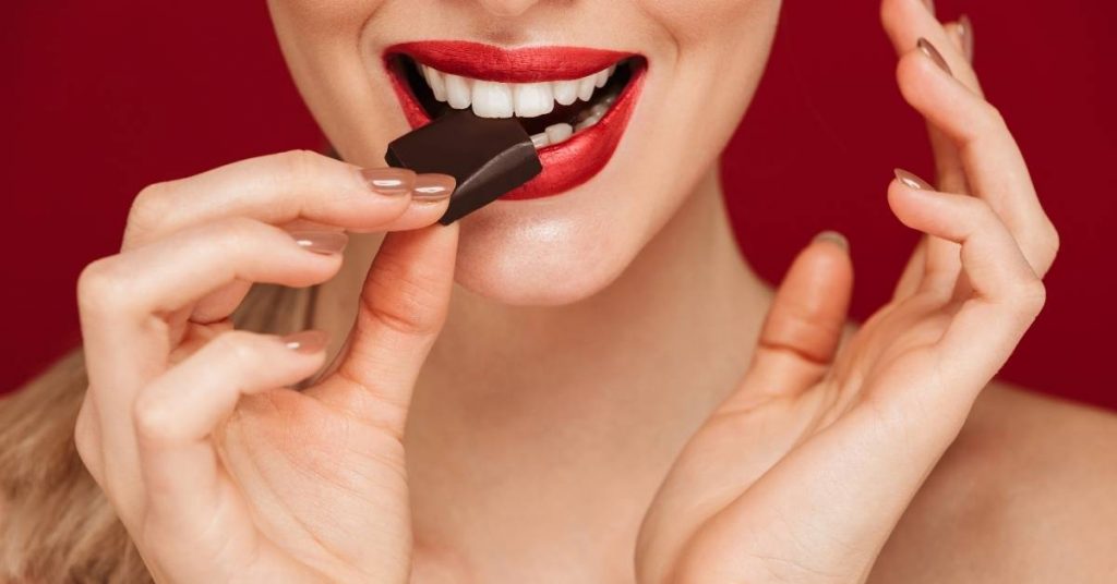 a person holding a chocolate bar near their mouth, demonstrating how sugar can affect teeth and cause dental pain
