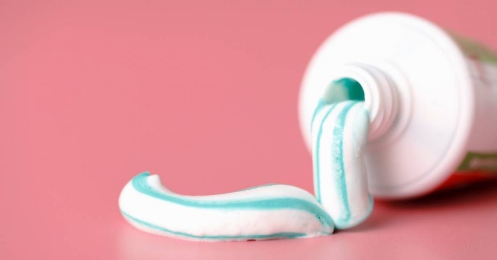 a tube of mint-colored fluoride toothpaste with a bent-out strip of foam for braces oral care on a pink background