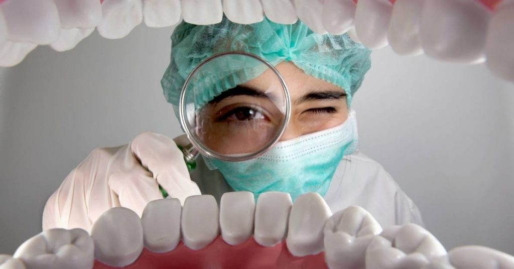 a dentist examining a patient’s teeth using a magnifying tool while wearing protective gear