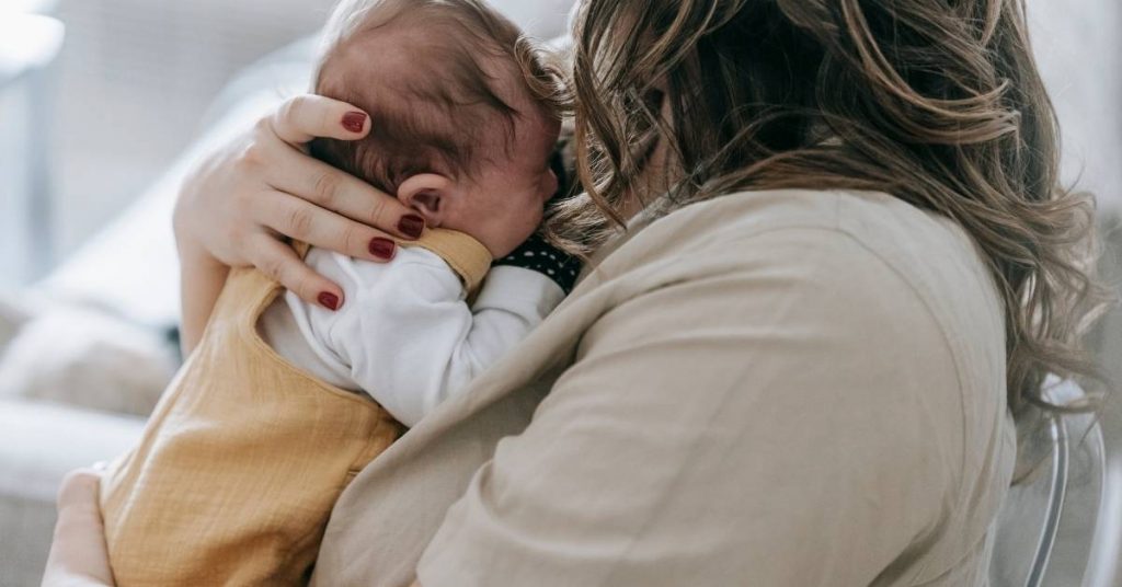a soothing adult holding a sleeping infant wrapped in a light-colored cloth, showing signs of teething discomfort.