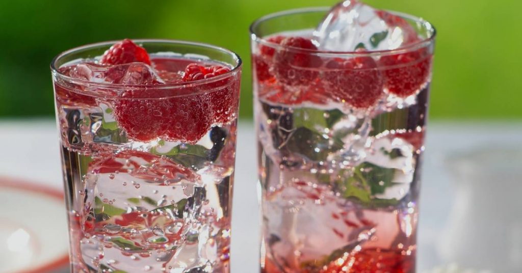 two tall glasses of refreshing raspberry-infused seltzer with ice and fresh mint leaves