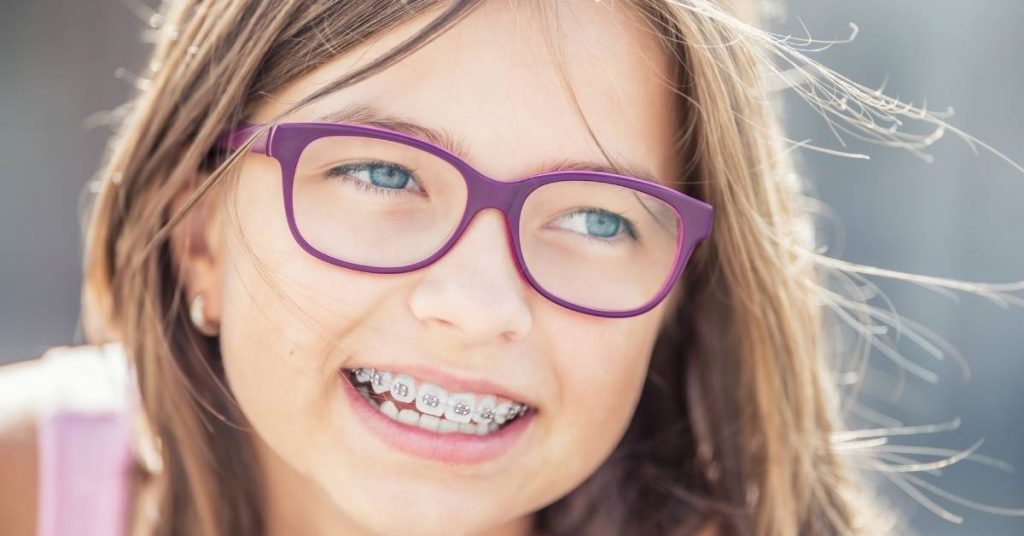a smiling young person wearing purple orthodontic glasses and metal braces on their teeth