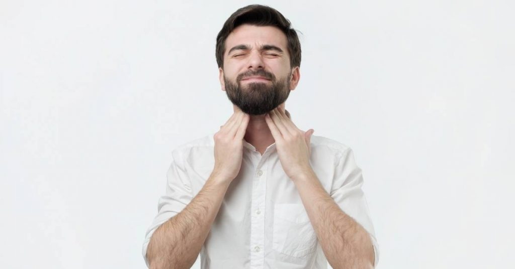 a person holding their chin and neck area, indicating possible swollen lymph nodes under the jaw.