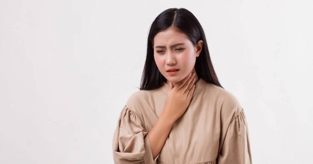 a person holding their throat, displaying discomfort or pain that may relate to canker sores or throat irritation.