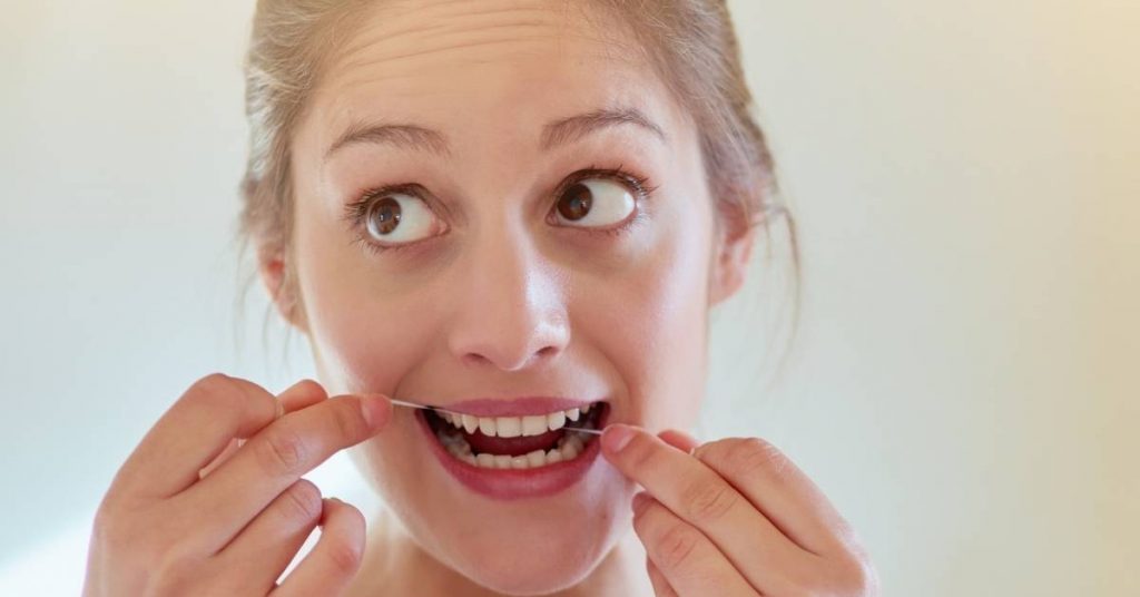 a person using DIY dental floss threaders incorrectly near their teeth, highlighting potential risks to dental health.