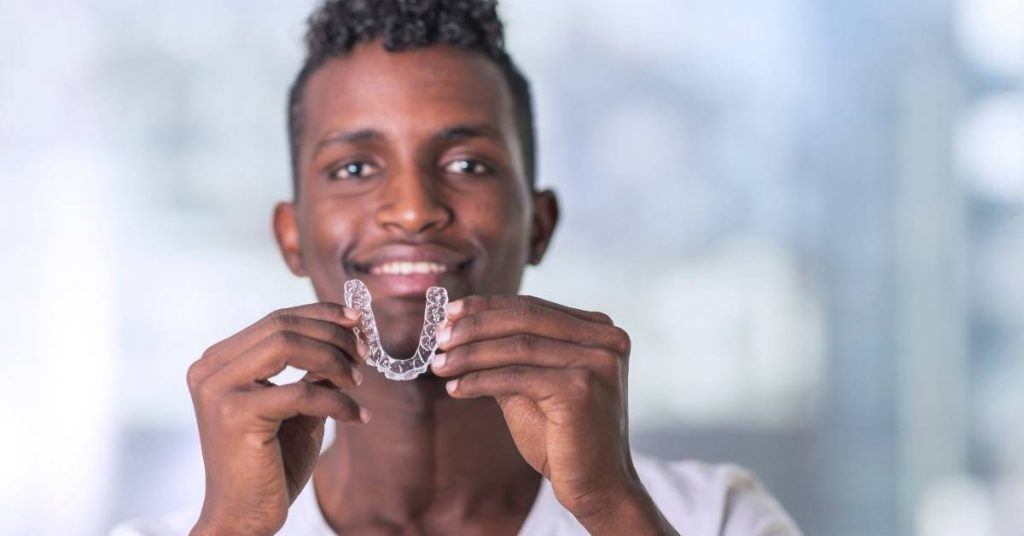 a person holding clear orthodontic aligners close to their smiling face, showcasing tooth alignment treatment.