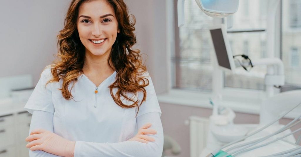 a smiling dental professional in a clinic with orthodontic equipment in the background
