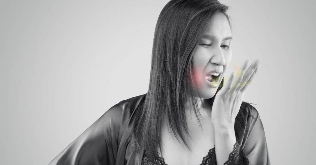 a person covering their mouth, appearing concerned about potential bad breath or halitosis.