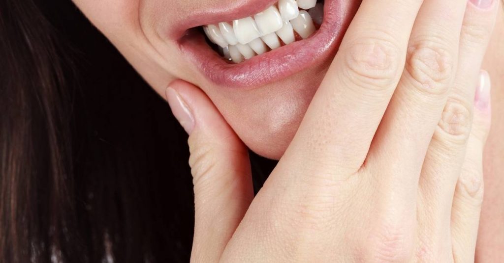 a person’s open mouth with visible teeth and gums while a hand gently supports the chin, highlighting gum area