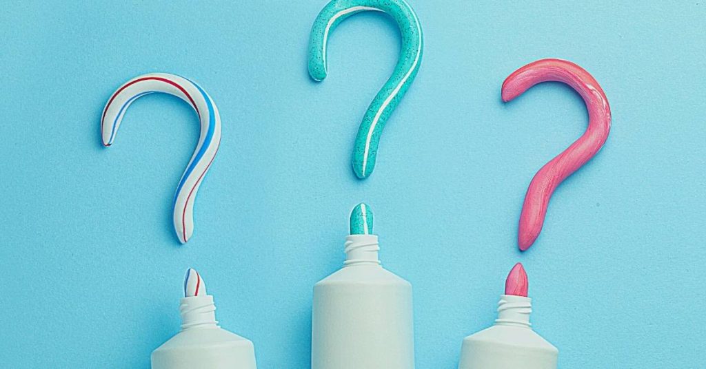 three toothpaste tubes with question-mark-shaped applicators in white, teal, and pink, highlighting uncertainty about toothpaste amount usage.