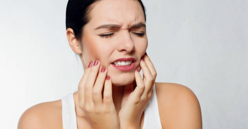 a person holding their jaw in pain, indicating symptoms of a gum abscess or tooth infection.