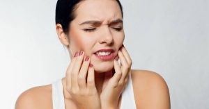 a person holding their jaw in pain, indicating symptoms of a gum abscess or tooth infection.