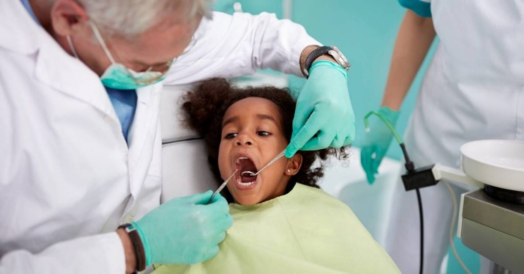 a young child at the dentist having their mouth examined for dental concerns, with a dental professional using a tool to inspect teeth.