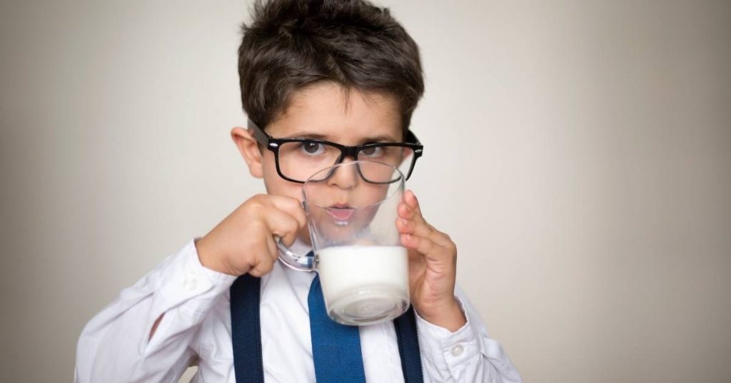 a young boy in glasses drinking milk from a glass while wearing a dress shirt and tie