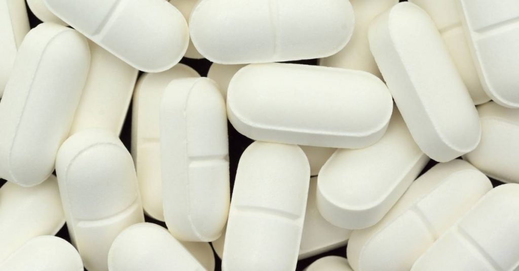 white oval and capsule-shaped pills in a scattered pile, commonly used for oral health supplements