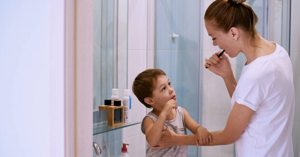 a woman assisting a young child with proper toothbrushing technique in a bathroom setting, emphasizing children's dental habits and oral hygiene.