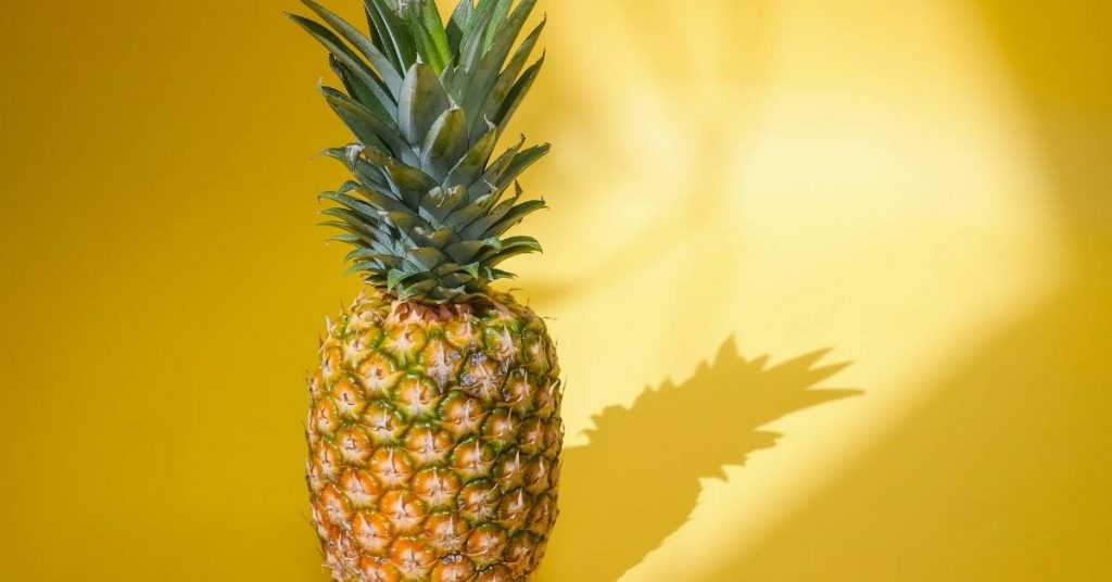 a ripe whole pineapple with green crown against a bright yellow gradient background