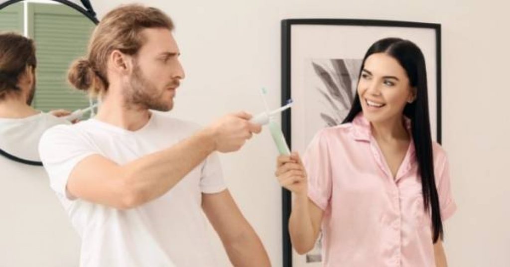 Photo of couple using electric toothbrushes to scrape tartar from their teeth