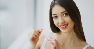 a smiling person holding a small whitening strip packet, showcasing a bright, confident expression.