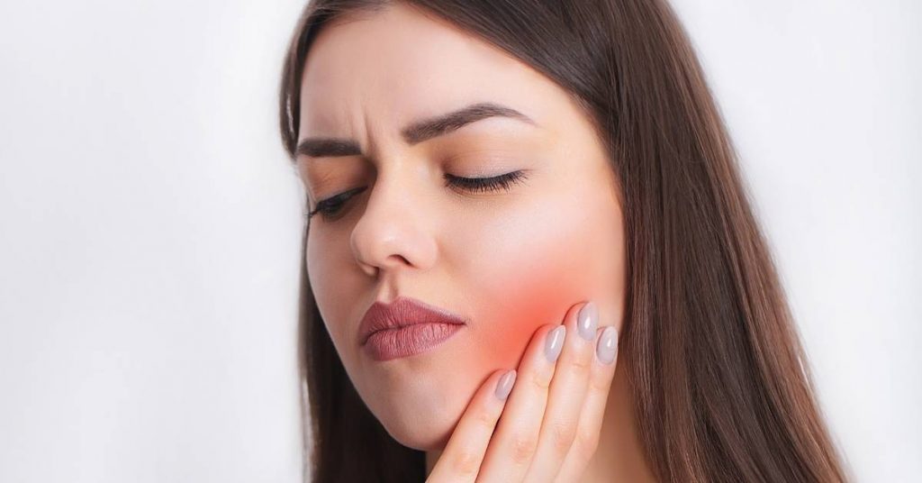 a person holding their jaw showing signs of wisdom tooth pain with visible gum inflammation and discomfort