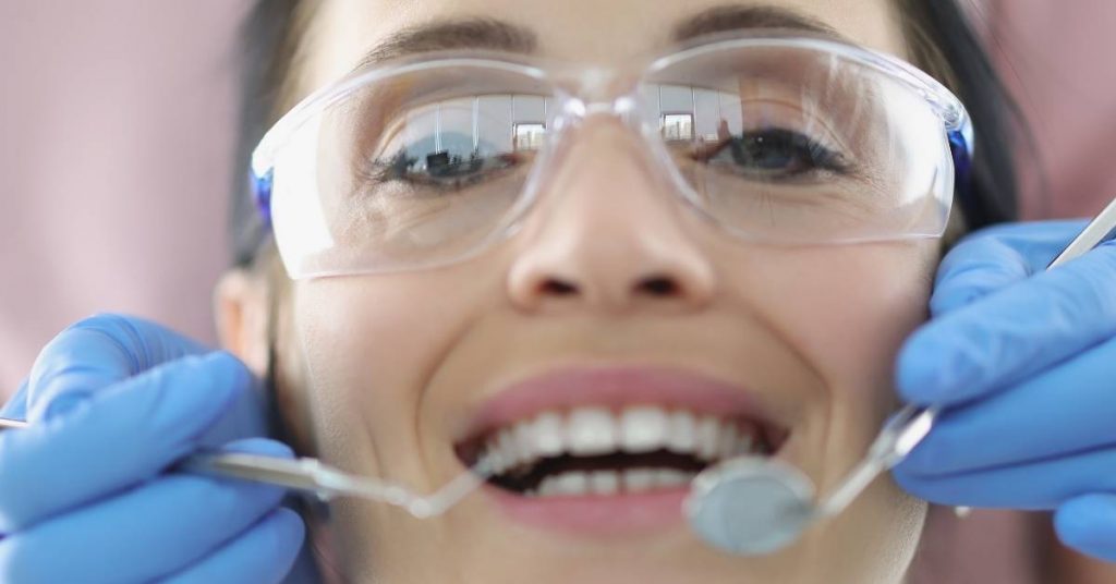 a dental specialist in protective gear performing an oral examination using dental tools near a patient’s teeth