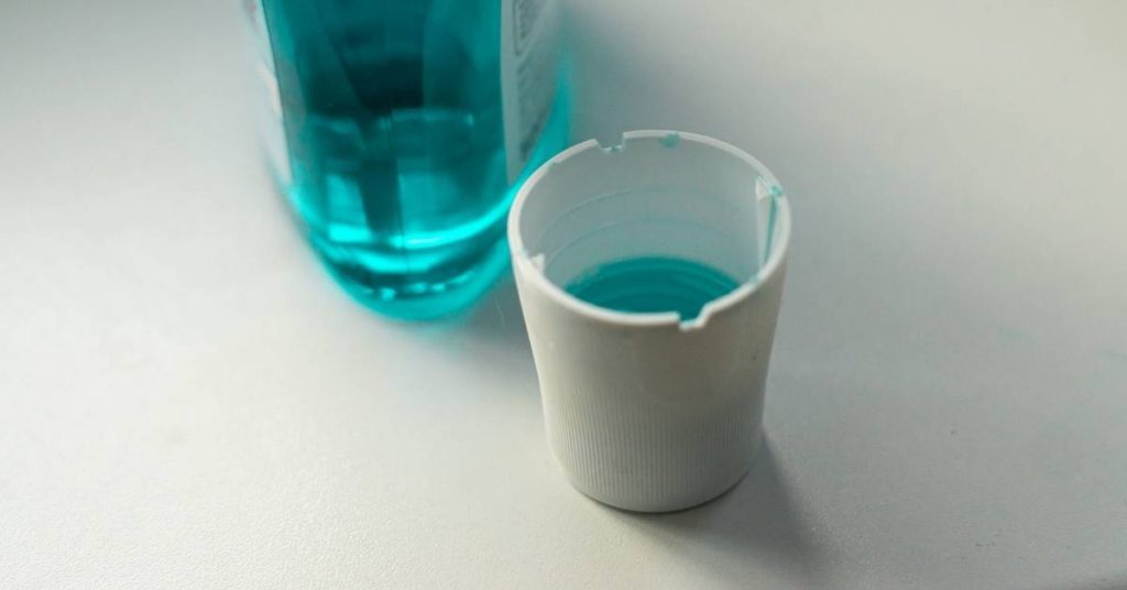 a clear turquoise mouthwash bottle with a small disposable cup containing mouthwash for gingivitis treatment