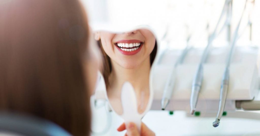 a happy patient smiling widely at a dentist’s reflection, showing healthy teeth after dental treatment
