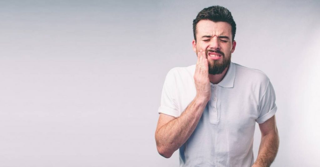 a man holding his cheek in apparent discomfort, suggesting dental pain or sensitivity.