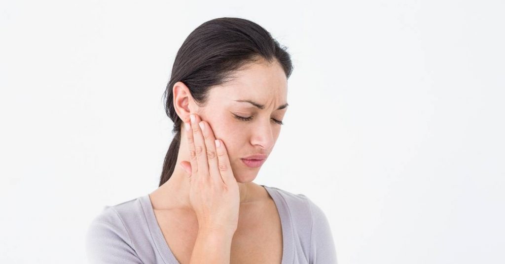 a person holding their jaw in discomfort, indicating potential post-operative numbness or pain after dental procedure.
