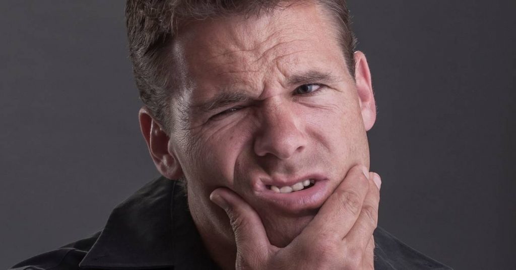 a person experiencing discomfort by holding their chin, indicating tooth pain.