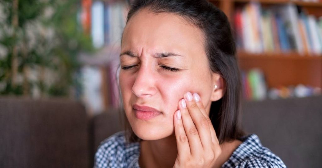 a person holding their jaw in discomfort, indicating tooth pain or dental inflammation.