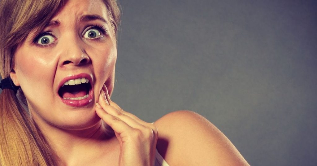 a person in distress clutching their jaw, indicating tooth or gum pain while chewing