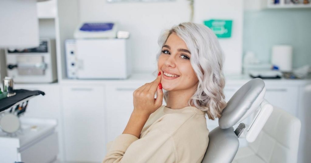 a person smiling in a dental chair holding a tongue depressor, post-procedure in a dental clinic setting