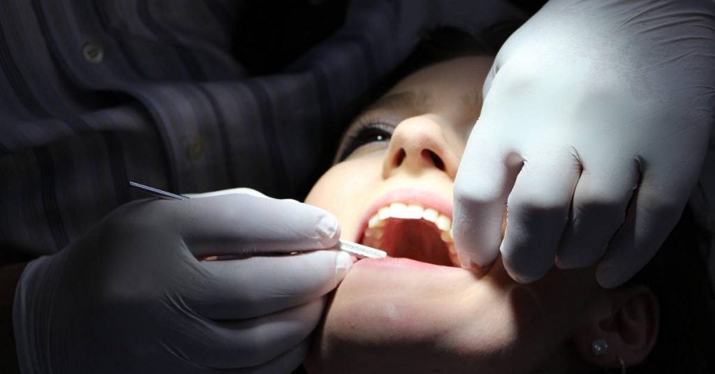 a dental professional examining a patient’s exposed tooth root during gum recession treatment with a dental probe.