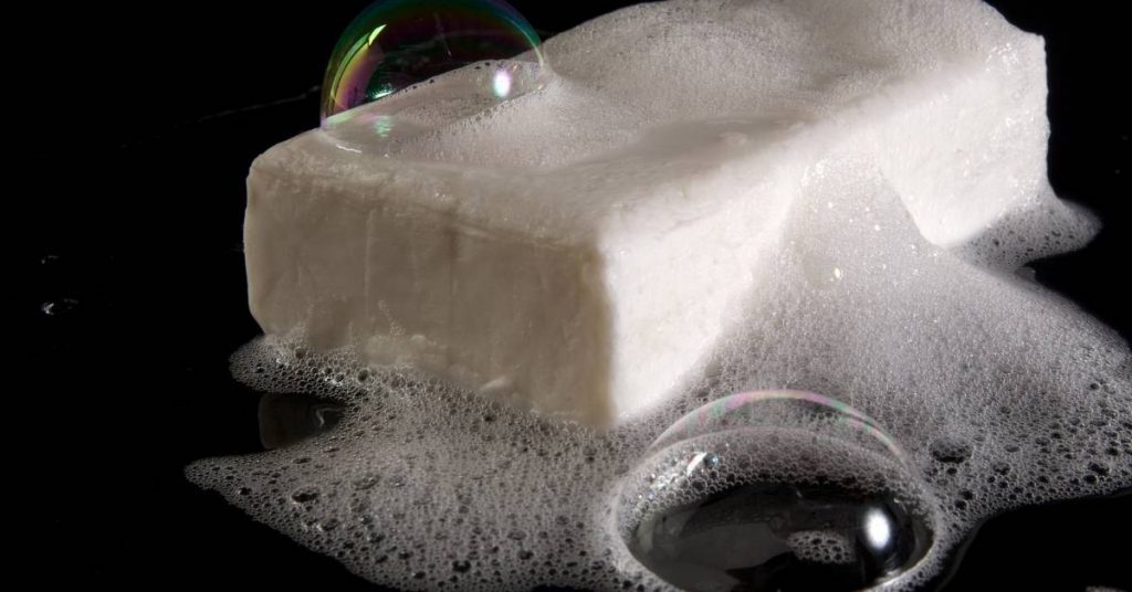 a block of soap dissolving in bubbly water with iridescent soap bubbles forming