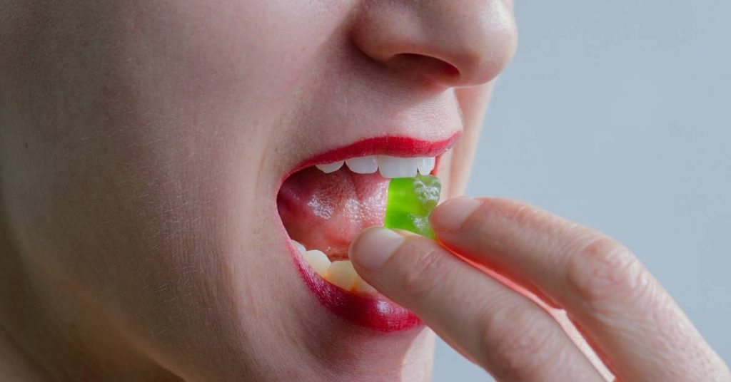 a person placing a green capsule or mint under their tongue while experiencing tooth sensitivity, with mouth open showing teeth and gums.