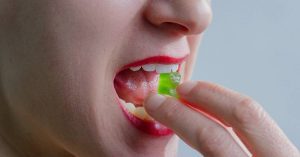 a person placing a green capsule or mint under their tongue while experiencing tooth sensitivity, with mouth open showing teeth and gums.