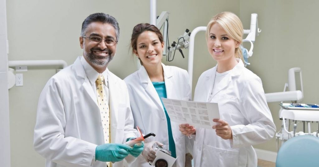 a smiling dental professional and two hygienists in a clinic holding dental tools and X-rays, showcasing root canal treatment preparation.