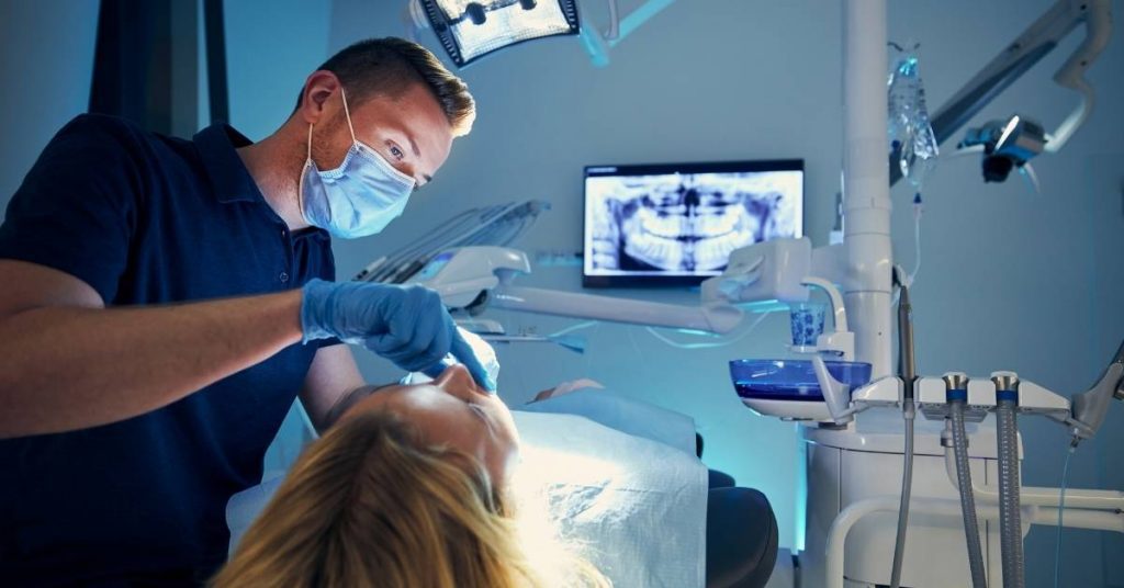 a dentist performing precise root canal treatment on a patient using dental tools and a dental X-ray screen for guidance