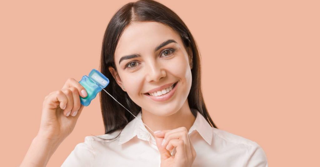 a smiling person holding a dental floss pick to remove food stuck between teeth