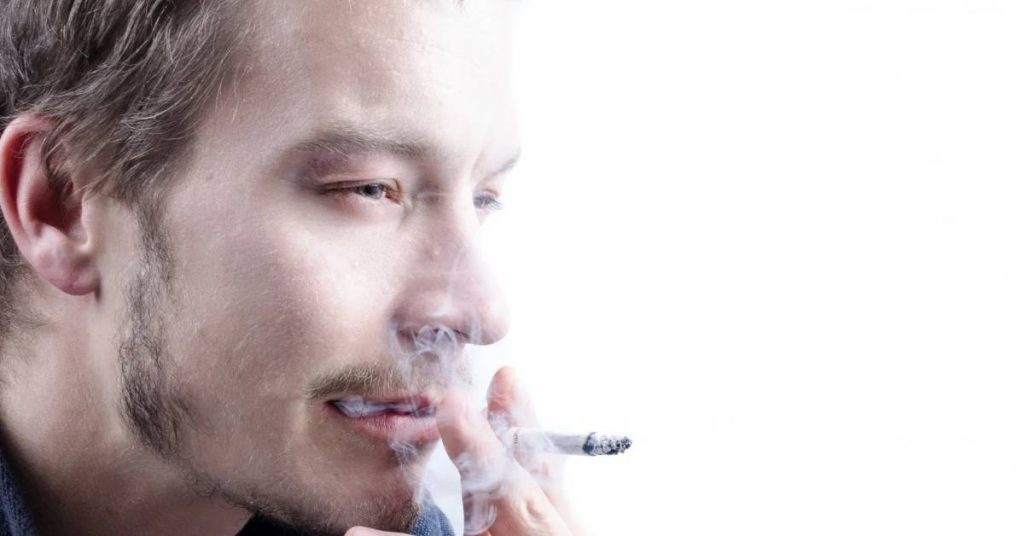 a person exhaling smoke, highlighting potential impacts on gum health and oral hygiene.