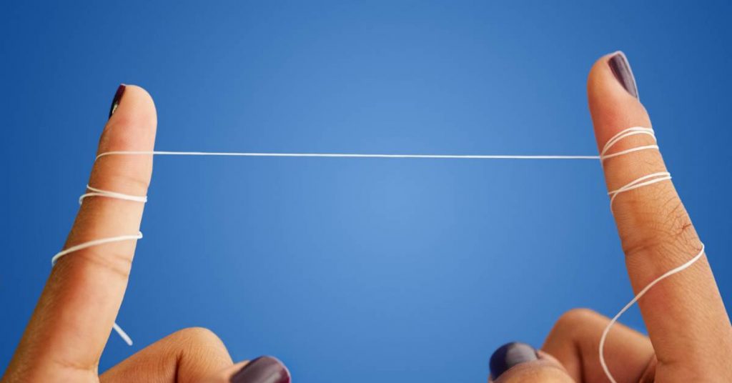 two fingers with dental floss stretched taut against a blue background, demonstrating proper flossing technique.