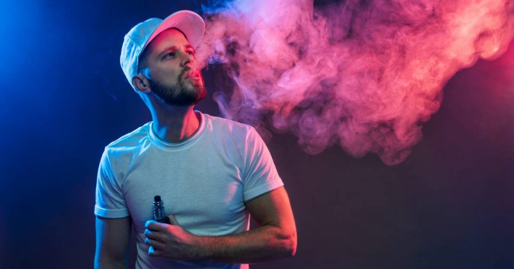 a person exhaling vaping vapor with a close-up of the cloud effect, holding an e-cigarette.