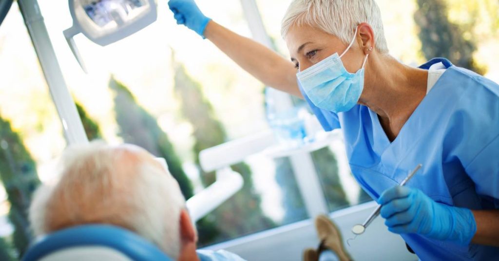 a dentist in protective gear examining a patient’s mouth with dental tools during a cracked tooth evaluation