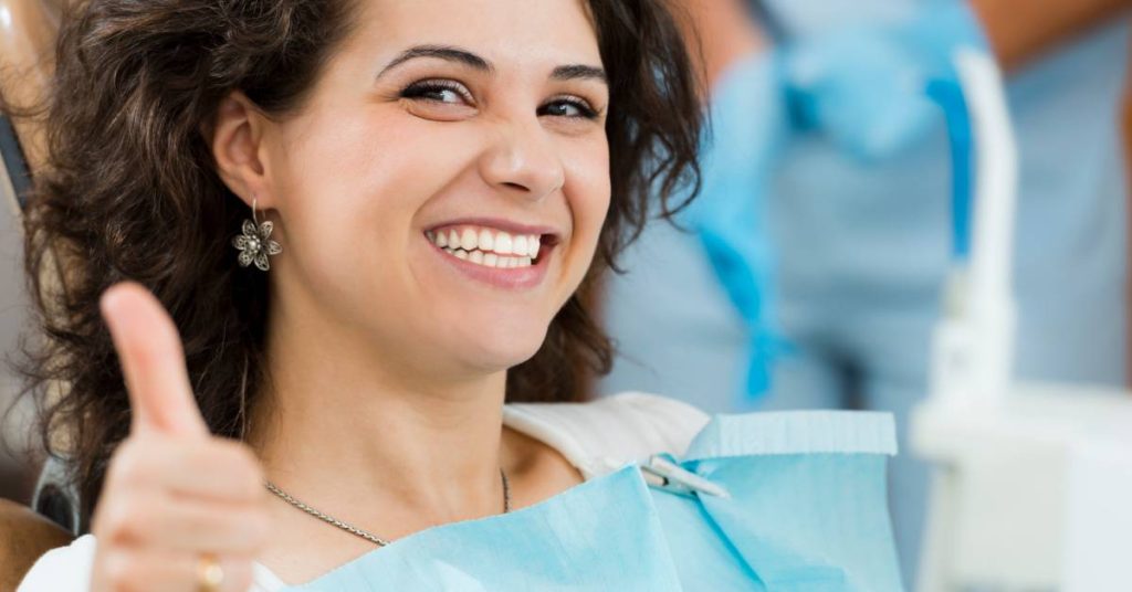a happy patient in dental bib giving a thumbs-up after a lumineers procedure