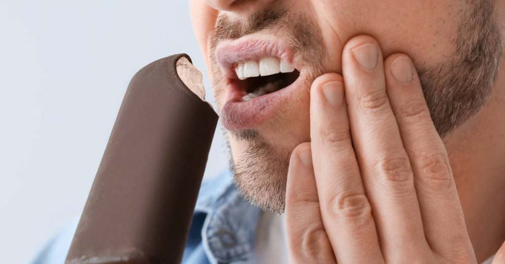 a person holding their cheek in pain while biting into a chocolate bar, illustrating tooth sensitivity from sugar.