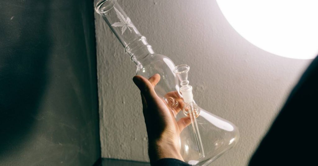 a hand holding a glass bong with a cannabis symbol etched on the top joint