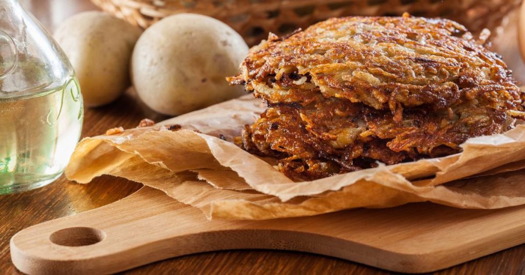 crispy homemade potato hash browns on parchment-lined wooden board with fresh potatoes and olive oil bottle nearby